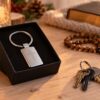 Metalowy brelok z krzyżem w czarnym etui, obok drewniany różaniec i klucze – prezent ze świętym patronem z grawerem